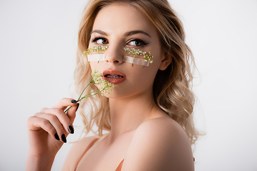 beautiful blonde woman in silk dress with wildflowers under eyes and near mouth isolated on white