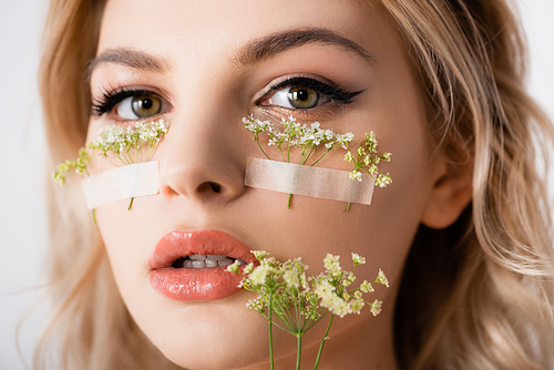 beautiful blonde woman with wildflowers under eyes and in mouth isolated on white