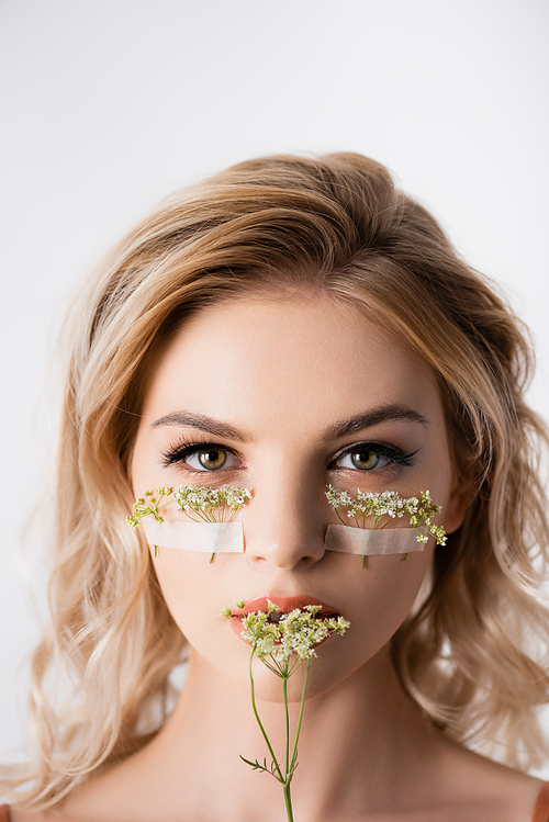 beautiful blonde woman with wildflowers under eyes and near mouth isolated on white