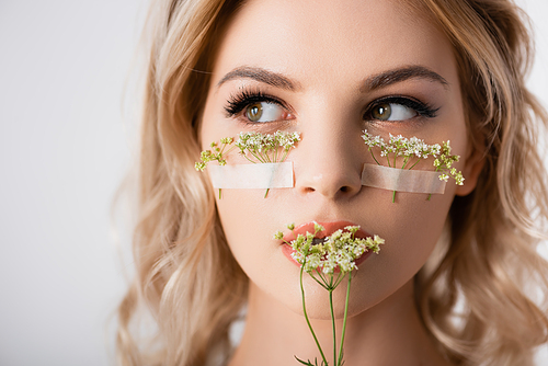 beautiful blonde woman with wildflowers under eyes and near mouth isolated on white