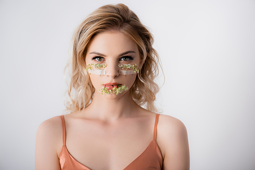 beautiful blonde woman in silk dress with wildflowers under eyes and in mouth isolated on white