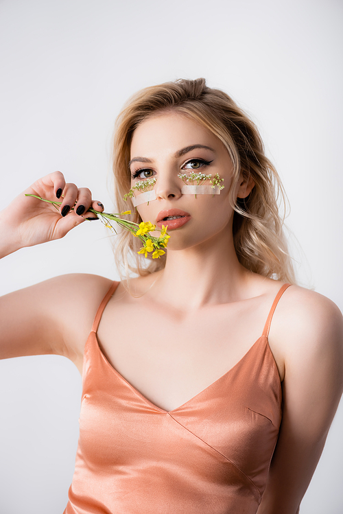 beautiful blonde woman in silk dress with wildflowers under eyes and near mouth isolated on white