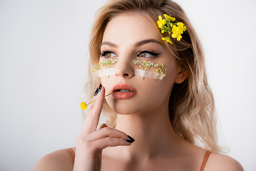 beautiful blonde woman with wildflowers under eyes and in mouth isolated on white