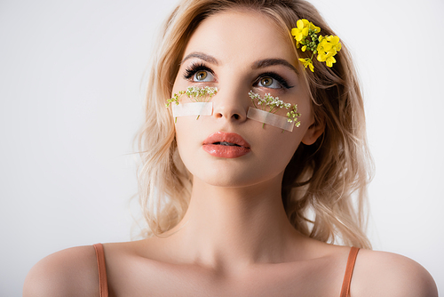 beautiful blonde woman with wildflowers under eyes looking away isolated on white
