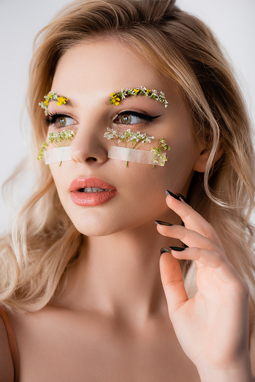 beautiful blonde woman with wildflowers under eyes looking away isolated on white