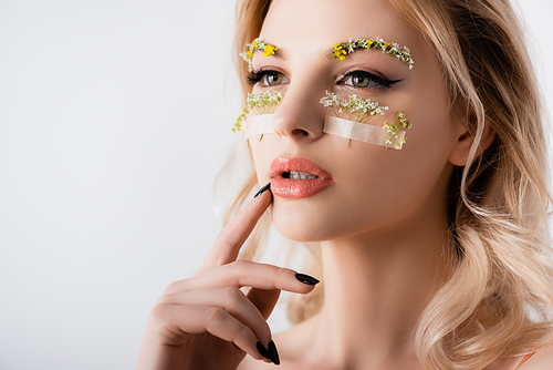 naked beautiful blonde woman in silk dress with wildflowers under eyes looking away isolated on white