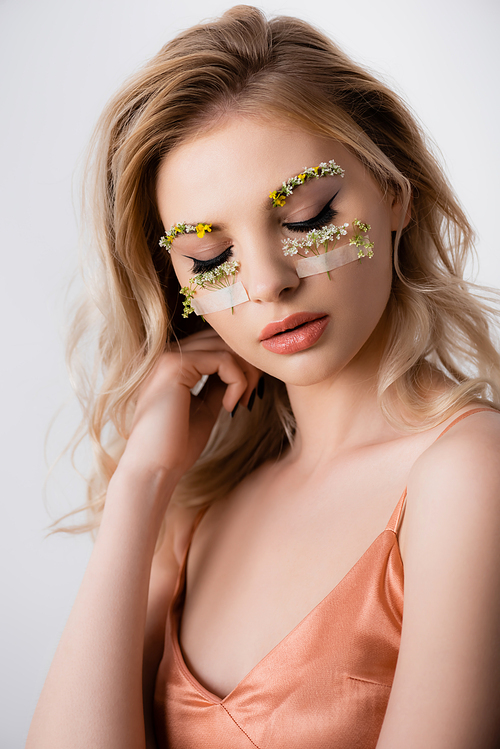 beautiful blonde woman in silk dress with wildflowers under eyes and closed eyes isolated on white