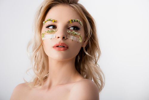 naked beautiful blonde woman with wildflowers under eyes looking away isolated on white