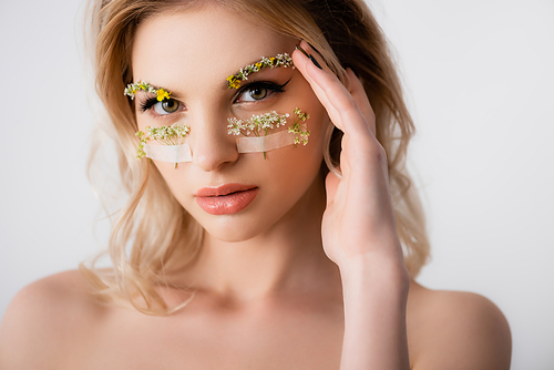 naked beautiful blonde woman with wildflowers under eyes and hand near face isolated on white