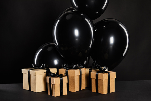 bunch of black balloons near gift boxes isolated on black, black Friday concept