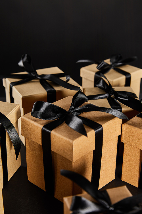 selective focus of cardboard gift boxes with black ribbons isolated on black, black Friday concept