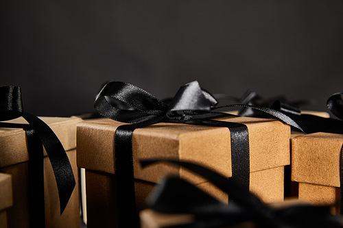 close up view of cardboard gift boxes with black ribbons isolated on black, black Friday concept