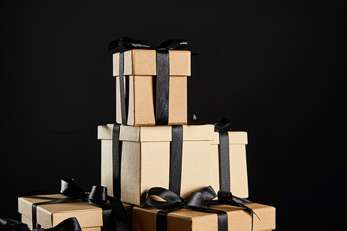 stack of cardboard gift boxes with black ribbons isolated on black, black Friday concept