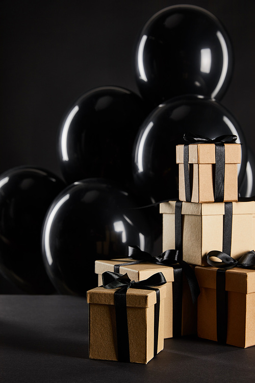 bunch of black balloons near stack of gift boxes isolated on black, black Friday concept
