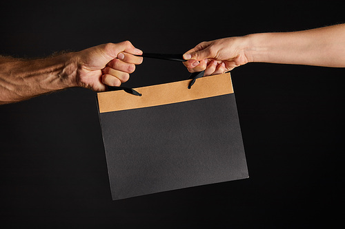 partial view of woman and man holding paper shopping bag isolated on black, black Friday concept