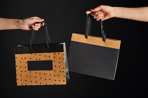 partial view of woman and man holding paper shopping bags isolated on black, black Friday concept