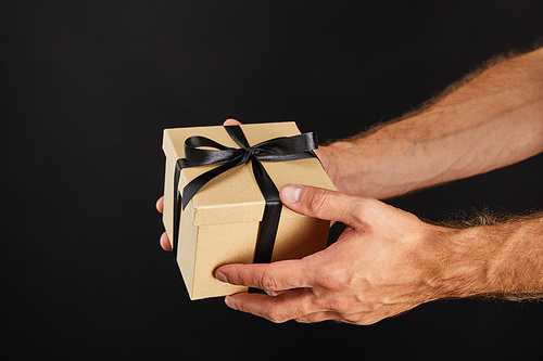 cropped view of man holding cardboard gift box with ribbon isolated on black, black Friday concept