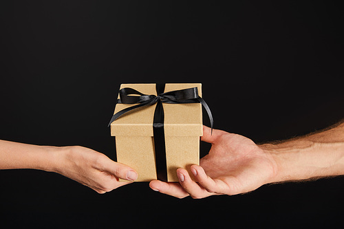 cropped view of man and woman holding cardboard gift box with ribbon isolated on black, black Friday concept