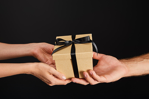 cropped view of man and woman holding cardboard gift box with ribbon isolated on black, black Friday concept