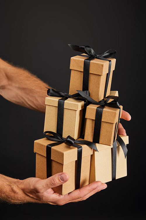 cropped view of man holding cardboard gift boxes with ribbons isolated on black, black Friday concept