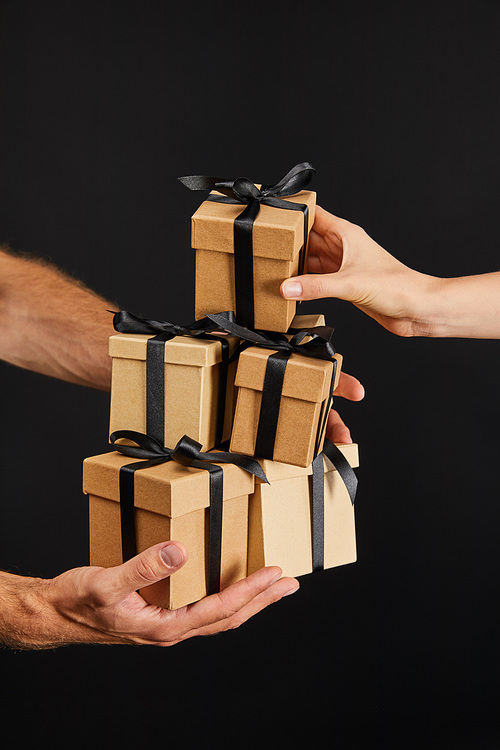 cropped view of man and woman holding cardboard gift boxes with ribbons isolated on black, black Friday concept