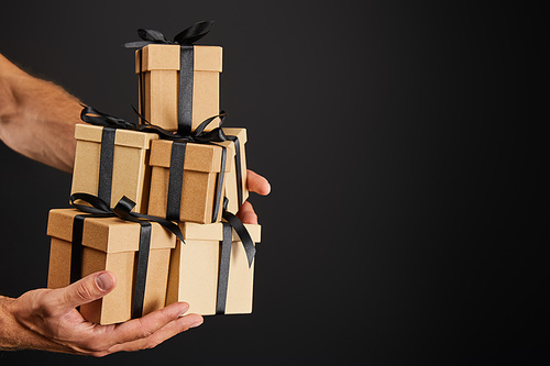 cropped view of man holding cardboard gift boxes with ribbons isolated on black, black Friday concept