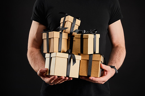 partial view of man holding cardboard gift boxes with ribbons isolated on black, black Friday concept