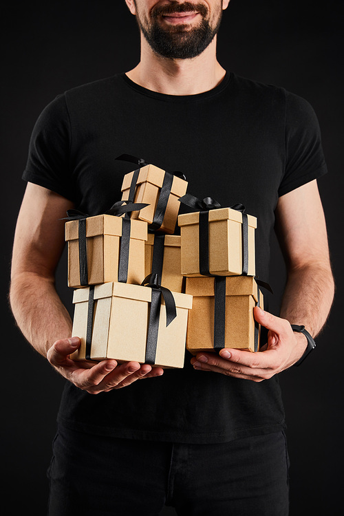 cropped view of smiling man holding cardboard gift boxes with ribbons isolated on black, black Friday concept