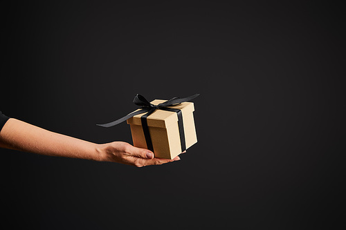 cropped view of woman holding cardboard gift box with ribbon isolated on black, black Friday concept