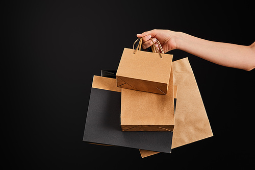 partial view of woman holding paper shopping bags isolated on black, black Friday concept