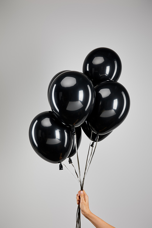 partial view of woman holding bunch of black balloons isolated on grey, black Friday concept