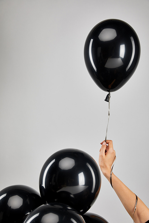cropped view of woman holding bunch of black balloons isolated on grey, black Friday concept
