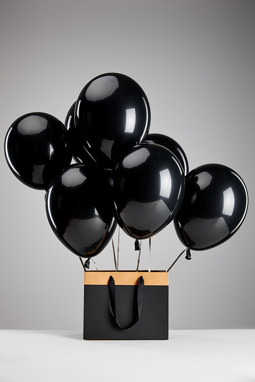 bunch of black balloons with paper shopping bag isolated on grey, black Friday concept