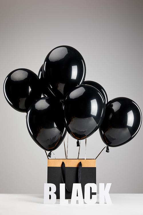 bunch of black balloons with paper shopping bag isolated on grey, black Friday concept
