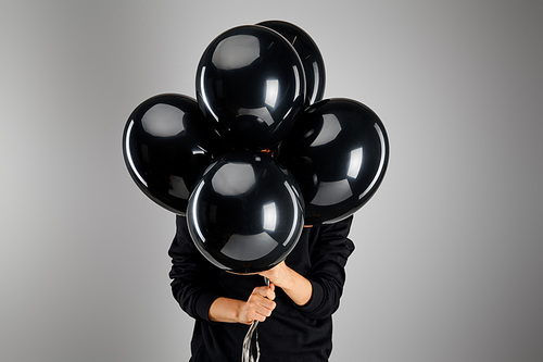 woman holding bunch of black balloons in front of face isolated on grey, black Friday concept