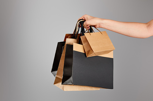cropped view of woman holding paper shopping bag isolated on grey, black Friday concept