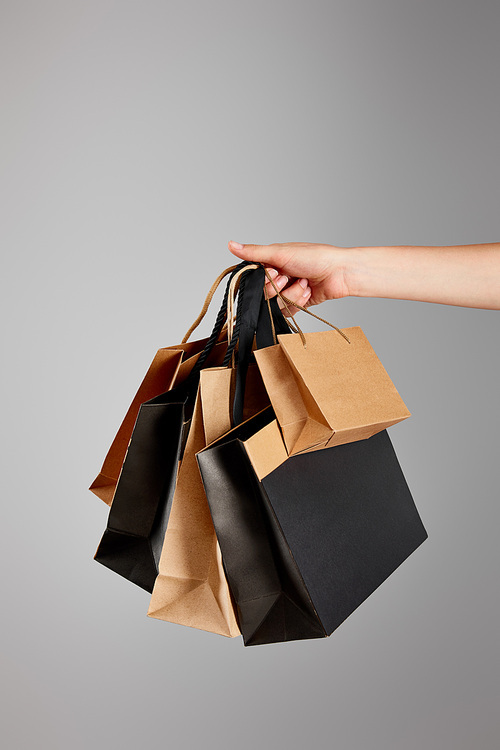 partial view of woman holding paper shopping bag isolated on grey, black Friday concept
