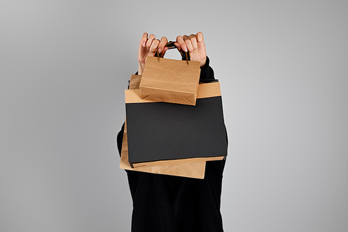 woman with obscure face holding paper shopping bags isolated on grey, black Friday concept