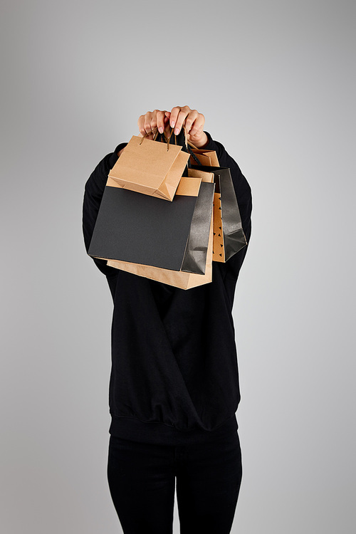 woman with obscure face holding paper shopping bags isolated on grey, black Friday concept