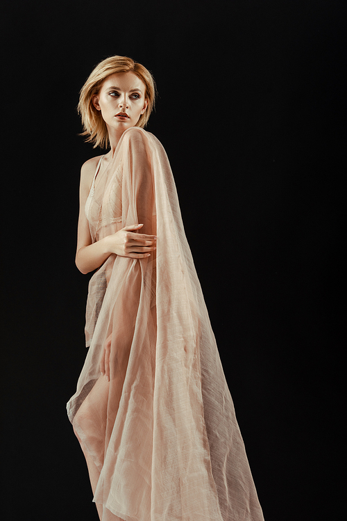 Blonde woman in underwear and chiffon cloth looking away isolated on black
