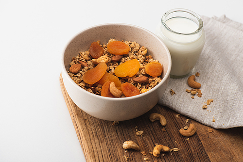 delicious granola with nuts, dried apricots and yogurt on wooden board on white background