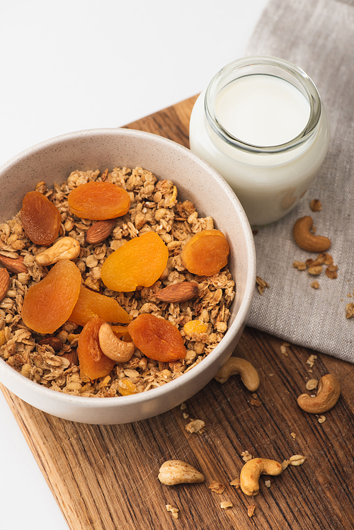 top view of delicious granola with nuts, dried apricots and yogurt on wooden board on white background