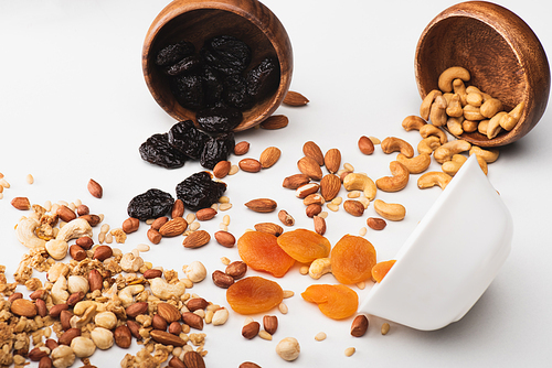 delicious granola with nuts and dried fruits scattered from bowls on white