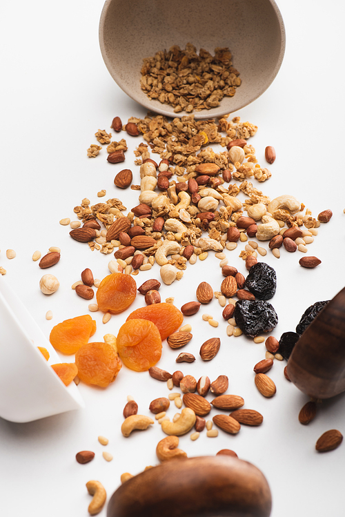 delicious granola with nuts and dried fruits scattered from bowls on white