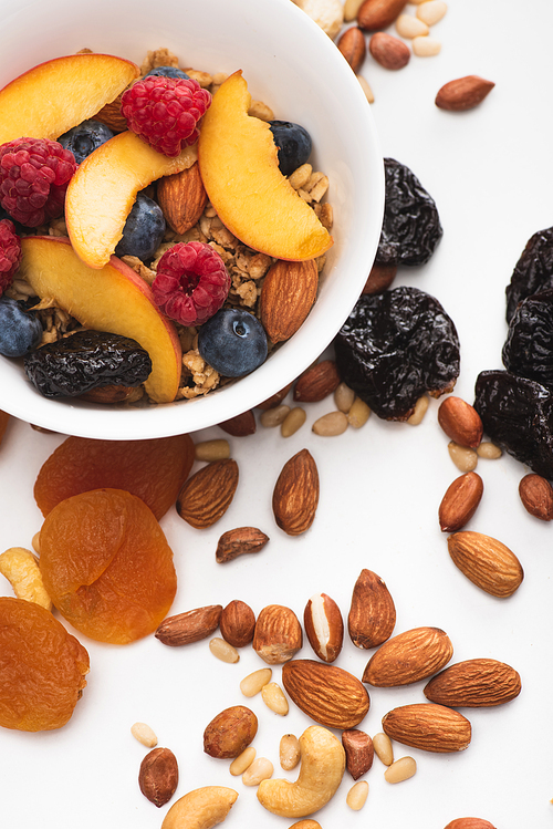 delicious granola with nuts, berries and fruits in bowl on white