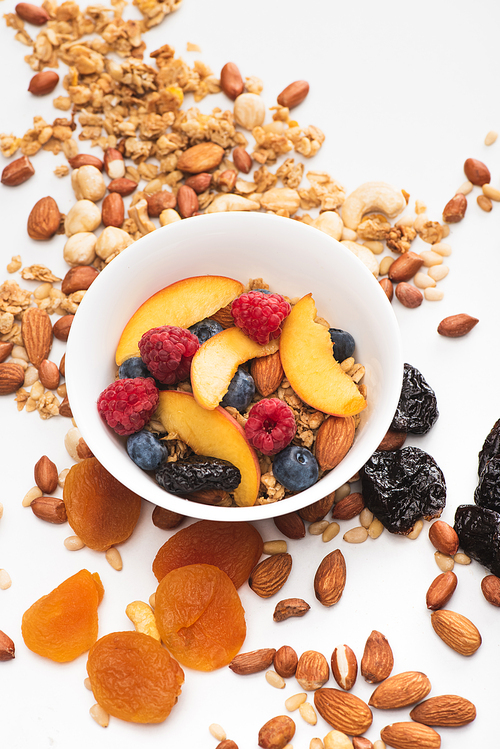 delicious granola with nuts, berries and fruits in bowl on white