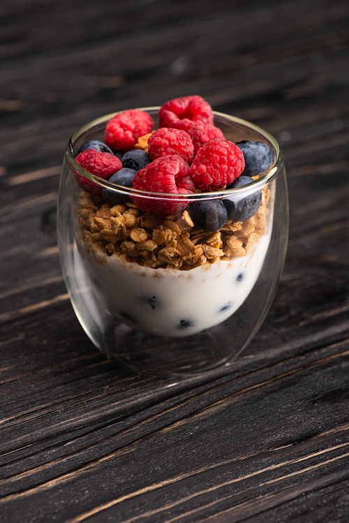 delicious granola with berries and yogurt in glass cup on wooden surface