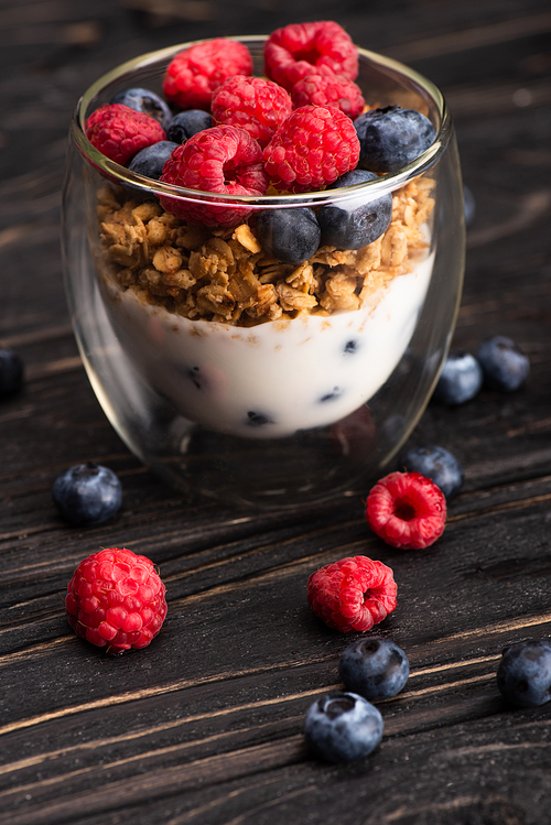 closeup of delicious granola with berries and yogurt in glass cup on wooden surface