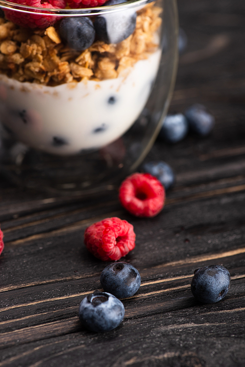 closeup of delicious granola with berries and yogurt in glass cup on wooden surface