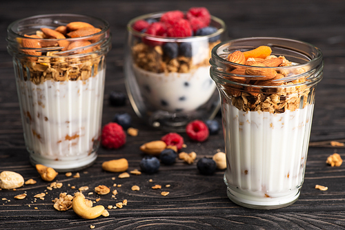 delicious granola with dried apricots, nuts and yogurt in glass cups on wooden surface on blurred background